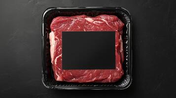 Raw beef steak on a black tray with a blank area for labeling or branding at a butcher shop photo