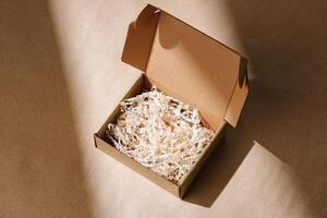 Open cardboard box with shredded paper packaging resting on a light brown surface illuminated by soft natural light photo