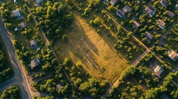 An aerial view of a vacant field surrounded by residential homes, capturing the lush greenery and shadows cast by trees during golden hour photo