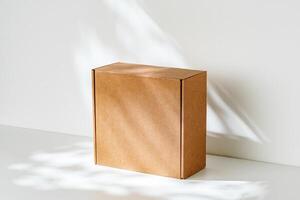 Simple brown cardboard box positioned on a white surface with soft angled shadows in natural light photo