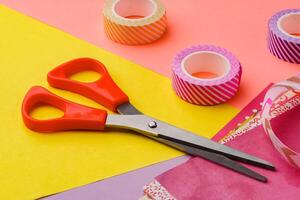 Scissors and decorative tape on colorful craft paper in a bright workspace photo