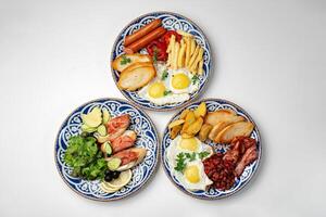 Traditional breakfast plates featuring eggs, sausages, and various accompaniments arranged artistically on a white background photo