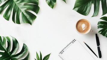 Relaxing workspace setup with tropical leaves, a coffee cup, and a notepad in a serene environment photo