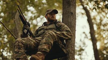 A hunter perched on a tree stand in a forest, observing surroundings with a rifle during the early morning hours photo