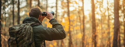 Hiker observing wildlife with binoculars in a tranquil forest during autumn sunset photo