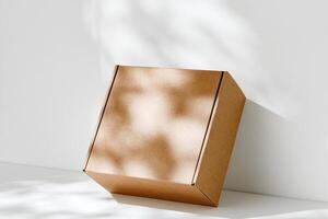 Simple brown cardboard box positioned on a white surface with soft angled shadows in natural light photo