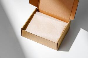 A small, empty cardboard box with unwrapped parchment resting inside on a bright, sunlit table photo