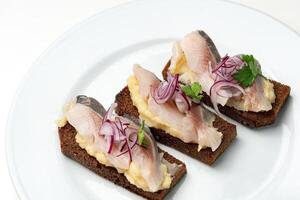 Open-faced sandwiches with herring and onions served on a white plate photo