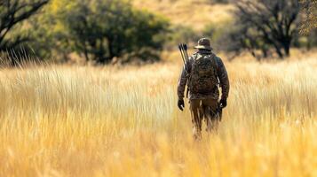 A hunter walks through tall grass with a bow and arrows, exploring the wilderness during a sunny day on open terrain photo