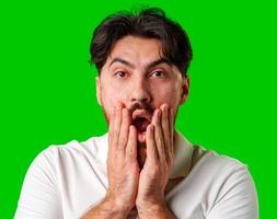 A man with a surprised expression holds his face while against a vibrant green background photo