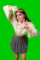 A young woman stands against a vibrant green screen, creating a finger frame with her hands as if visualizing a composition or focusing on a specific view. photo