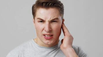 Otitis. Studio portrait of young man suffering from ear pain, close up, grey background video