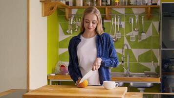 ein jung Frau Scheiben ein Orange im ein zeitgenössisch Küche während vorbereiten zum Frühstück. video