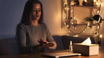 A young woman sits at a table, deep in thought, with a laptop and a tissue box nearby, illuminated by soft warm lights. video