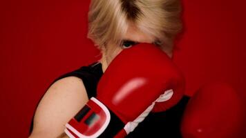 A determined young athlete practices their boxing skills with red gloves, focusing intently on their form against a bright red background that enhances the energy of the training session. video