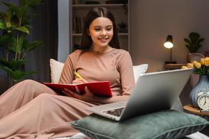 Young girl, teenager taking notes while attending online class at home photo