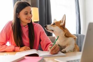 Smiling student taking notes while petting her corgi dog photo