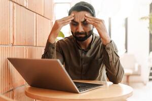 Stressed Indian businessman using laptop working, headache, something wrong, failed business photo