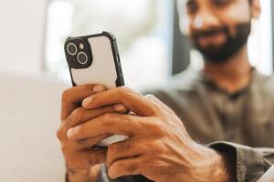 Smiling Indian man holding using smartphone browsing internet, selective focus, closeup on hands photo
