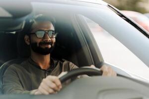 Handsome bearded man with sunglasses smiling while driving car photo