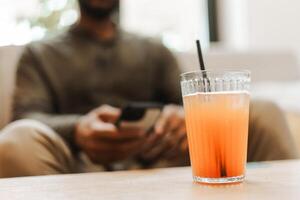 Man relaxing with smartphone and refreshing cold drink on table photo