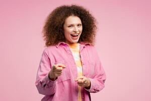entusiasmado, sonriente mujer con Rizado pelo vistiendo casual ropa señalando dedos, mirando a cámara foto