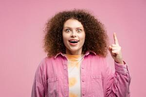 atractivo lleno de alegría mujer con Rizado pelo vistiendo elegante camisa participación dedo arriba, teniendo bueno idea foto