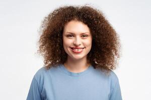 atractivo, contento joven mujer con Rizado pelo vistiendo elegante verano azul t camisa mirando a cámara foto