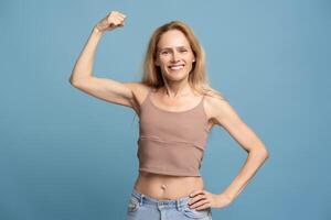 Strong, smiling woman wearing tank top showing her biceps looking at camera on blue background photo