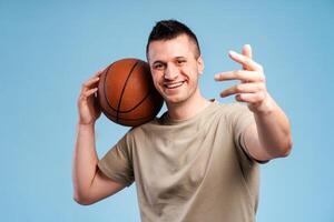 Handsome sportsman holding basketball and showing number three with fingers on blue background photo