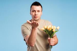 Handsome young man holding bouquet of flowers in his hand, blowing an air kiss photo
