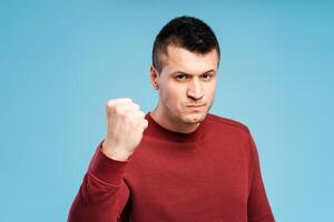 Angry, irritated young man in red sweatshirt showing clenched fist, showing anger. Conflict concept photo