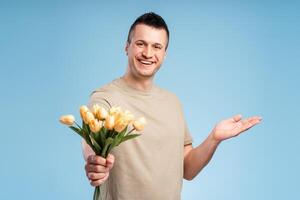 Handsome, smiling man looking at camera holding bouquet of flowers and pointing to copy space photo