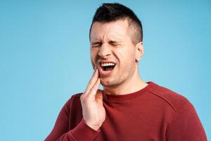 Middle aged man with closed eyes having teeth pain, standing on blue background photo