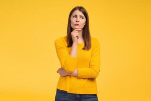Serious middle aged woman looking away, choosing something, standing isolated on yellow background photo
