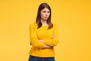 Offended, beautiful woman with arms crossed looking at camera standing isolated on yellow background photo