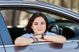 Happy woman looking at camera from car window and smiling while relaxing photo