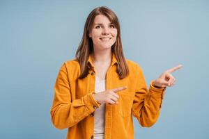 hermoso, sonriente medio Envejecido mujer vistiendo amarillo camisa, señalando con dedos a espacio foto