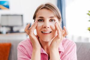 Beautiful, smiling woman with under eye patches on her face, moisturizing, looking at camera photo