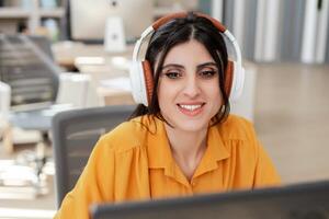 Smiling woman confident programmer in headphones using computer, working online looking at screen photo
