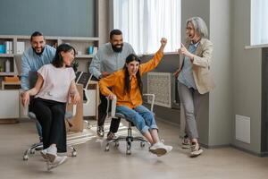 Happy office workers having fun riding on chairs in modern office photo