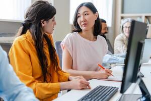 Two female programmers discussing code on computer in busy office photo