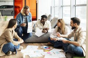 Group of diverse, multiracial team discussing documents and graphs on floor photo