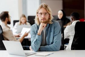 Handsome project manager sitting at desk with team working in background photo