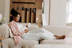 Pregnant woman relaxing on sofa drinking tea photo