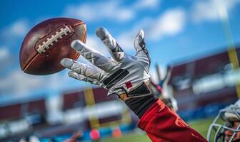 A football player's hands catching the ball mid-air, with the field and goalposts in the background photo