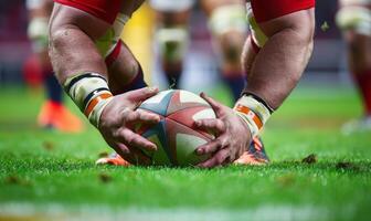 A rugby player's hands gripping the ball, with the field and players in the background photo