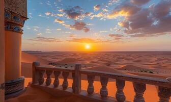 A vast desert landscape with sand dunes and a setting sun, viewed from a balcony with Arabian architectural elements photo