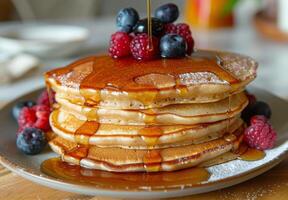 A stack of fluffy pancakes drizzled with maple syrup and topped with fresh berries photo