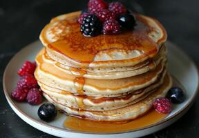 A stack of fluffy pancakes drizzled with maple syrup and topped with fresh berries photo